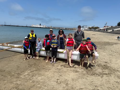 scouts and parents with outrigger canoe, standing on beach